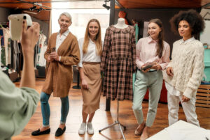 Group photo. Young woman making a photo of her fashionably dressed collaborateurs of different age and race in a big bright creative workshop